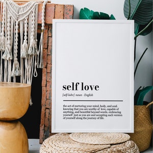 May include: A black and white printable wall art print with the definition of self-love. The print is framed in a white frame and is hanging on a brick wall.