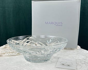 Può includere: Una ciotola di cristallo trasparente con un motivo geometrico, posta davanti a una scatola bianca con la scritta "MARQUIS by WATERFORD". È presente anche una piccola carta con il logo Marquis. La ciotola è probabilmente per scopi decorativi o di servizio.