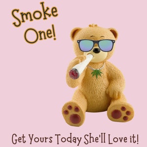 May include: A tan teddy bear figurine wearing sunglasses and a marijuana leaf necklace, holding a lit joint. The text "Smoke One!" and "Get Yours Today She'll Love it!" are displayed on a pink background.