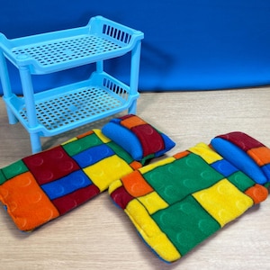 May include: A light blue plastic two-tiered shelf unit with a grid pattern. Two colorful rectangular pet beds with a patchwork design of red, blue, yellow, and orange blocks are in front of the shelf.
