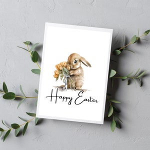 May include: A white card with a watercolor illustration of a brown bunny holding a bouquet of orange flowers. The text "Happy Easter" is written in black cursive below the bunny.