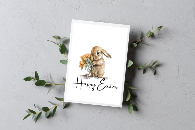 May include: A white card with a watercolor illustration of a brown bunny holding a bouquet of orange flowers. The text "Happy Easter" is written in black cursive below the bunny.