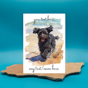 May include: Greeting card with a watercolour painting of a black dog running on a beach. The card has the text "your text here" at the top and "any text/name here" at the bottom. The background shows the ocean and sand.