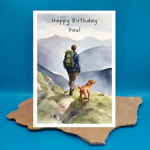 May include: A watercolour birthday card featuring a man with a backpack and a dog walking on a mountain path. The card says "Happy Birthday Paul".