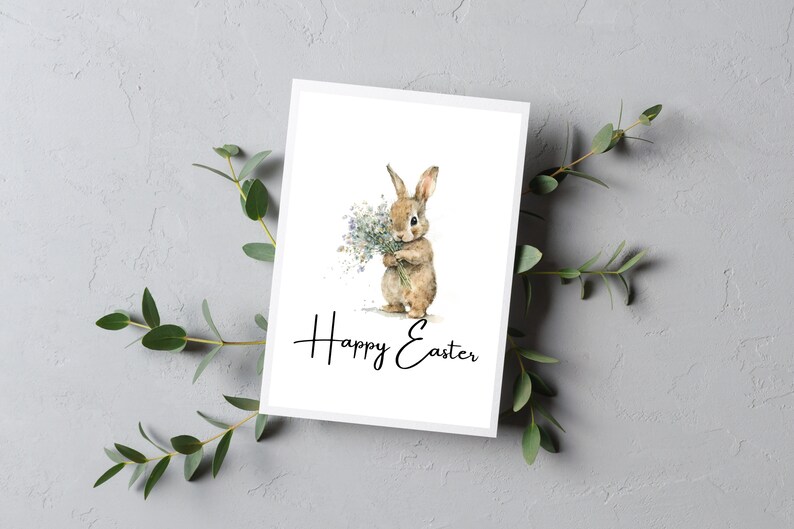May include: A white card with a watercolor illustration of a brown bunny holding a bouquet of white flowers. The text "Happy Easter" is written in black cursive below the bunny.