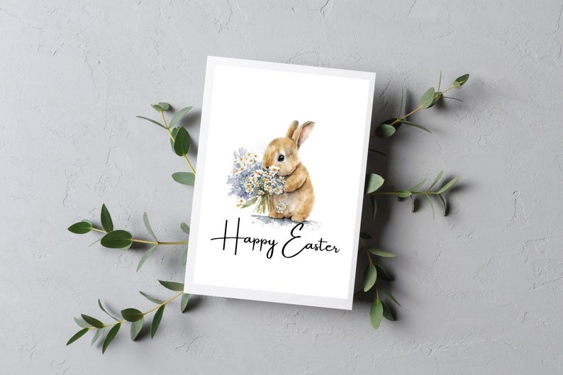 May include: A white card with a watercolor illustration of a brown bunny holding a bouquet of purple and white flowers. The text "Happy Easter" is written in black cursive below the bunny.