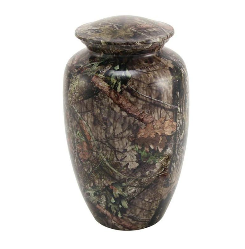 May include: A brown and green camouflage urn with a lid. The urn is made of metal and has a smooth finish.