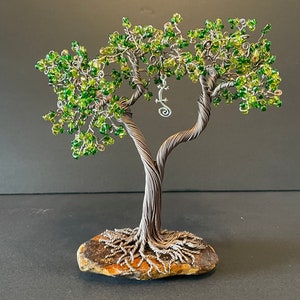 May include: A handcrafted wire tree sculpture with a twisted trunk and branches adorned with green beads, resembling leaves. A small metal lizard is suspended from the branches. The tree is rooted in a natural stone base.