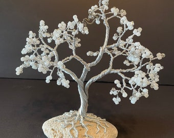 Twisted silver wire tree with white beads displayed on a white rock