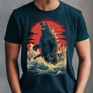 以下が含まれることがあります： ネイビーブルーのTシャツ。ゴジラのグラフィックが特徴です。デザインは、海から現れるゴジラ、赤い太陽、都市のスカイラインを描いています。グラフィックは黒、グレー、赤、ベージュの色合いを使用しています。