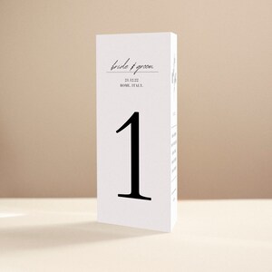 May include: White table number card with black calligraphy text that reads "bride & groom" and "21.12.22 ROME, ITALY." The number "1" is in large black font.