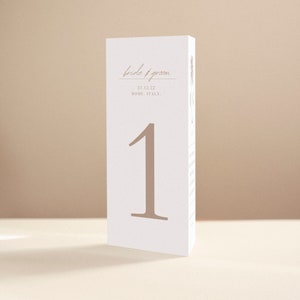 May include: White table number card with the number "1" in a brown font. The card also has the text "bride & groom" in a brown font, the date "21.12.22", and the location "ROME, ITALY."