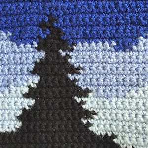 May include: A crochet tapestry featuring a landscape scene with a large black pine tree in the foreground. The background displays layers of light blue and medium blue yarn, topped with a dark purple sky containing small white stitched stars.