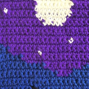 May include: A crochet fabric piece featuring a night sky scene with a large white circular moon and small white star accents set against a deep purple background, transitioning into a dark blue and light blue landscape with a black silhouette.