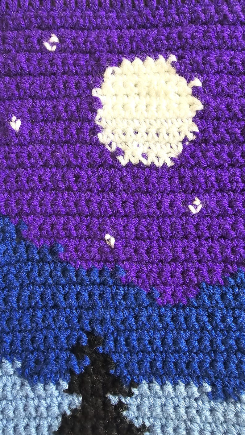 May include: A crochet fabric piece featuring a night sky scene with a large white circular moon and small white star accents set against a deep purple background, transitioning into a dark blue and light blue landscape with a black silhouette.
