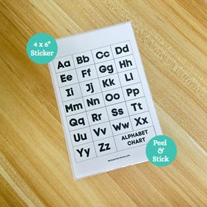 May include: A white alphabet chart sticker, 4 x 6 inches, with black uppercase and lowercase letters arranged in a grid. The sticker has a peel and stick feature and is on a wooden surface.