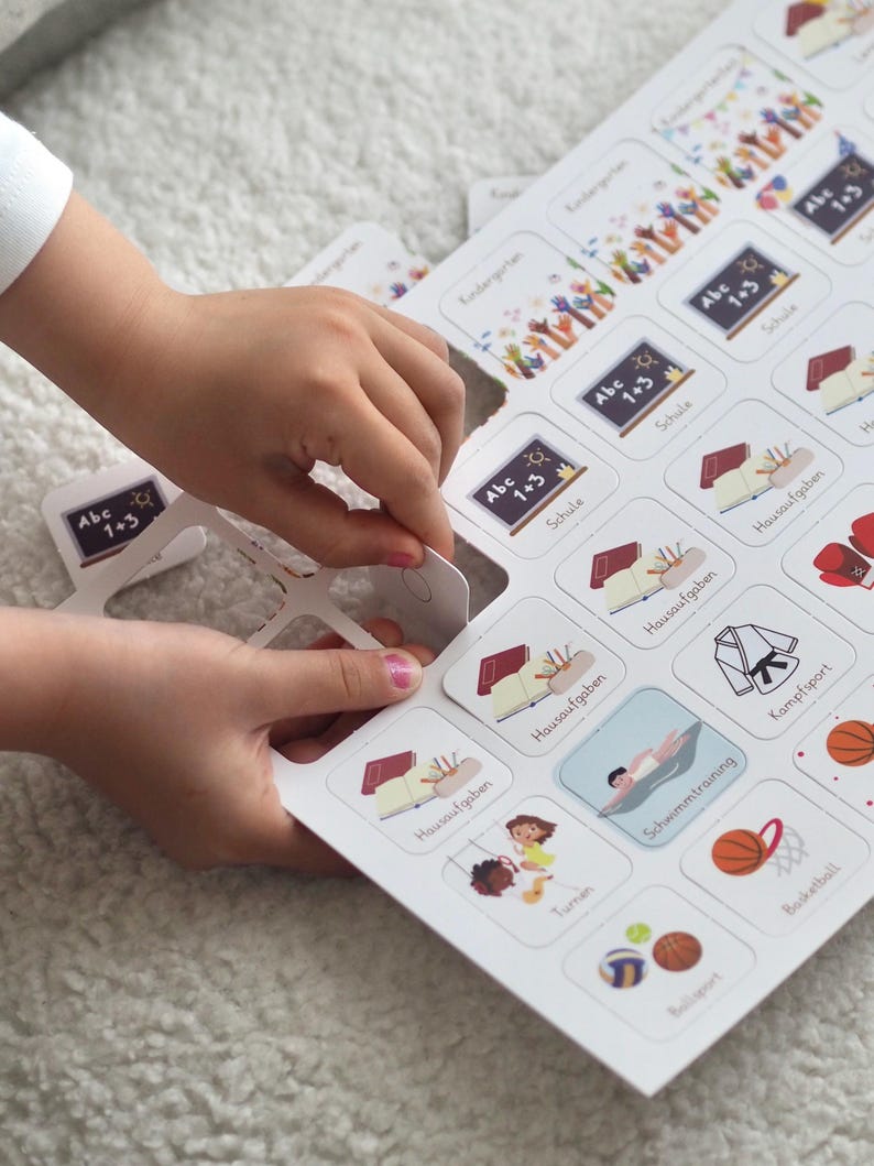 May include: A white board game with colorful illustrations and text in German. The game features cards with images of activities like school, swimming, and sports. The text on the cards includes "Abc 1+3", "Schule", "Hausaufgaben", "Schwimmtraining", "Kampfsport", "Turnen", "Ballsport", and "Basketball".
