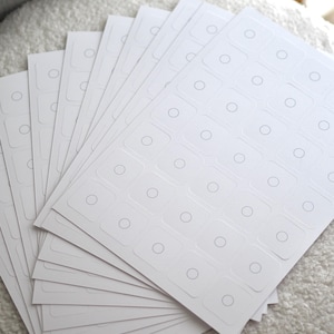 May include: A stack of white sheets with multiple rows of small, round, gray circles printed on each sheet. The sheets are arranged in a fan shape.