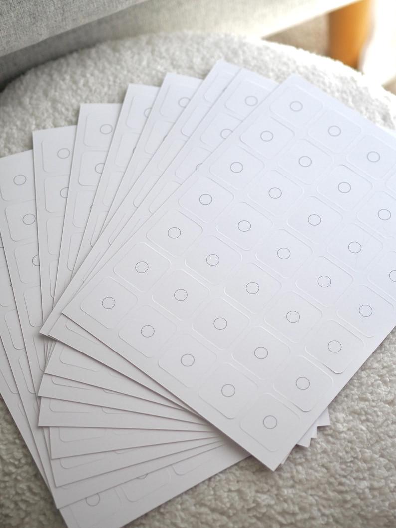 May include: A stack of white sheets with multiple rows of small, round, gray circles printed on each sheet. The sheets are arranged in a fan shape.