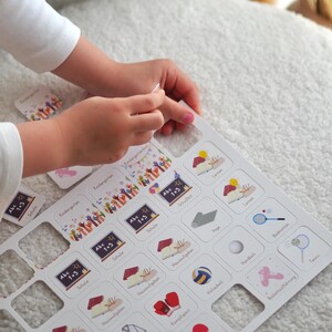 May include: A white board with a grid of squares, each containing an image and text. The images depict various activities, such as school, sports, and hobbies. The text includes words like "Kindergarten", "Schule", "Hausaufgaben", "Yoga", "Kampfsport", "Volleyball", "Handball", "Badminton", "Tennis", and "Ballett/Tanz/Figuren".