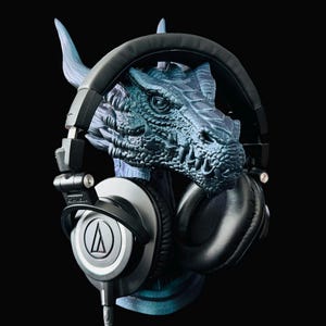 May include: Black headphones with a blue dragon-shaped stand. The headphones have a silver logo on the earcups.