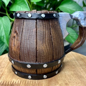 May include: A wooden beer stein with a metal axe handle. The stein is brown with black metal bands and silver rivets. The axe handle is silver with a black metal band.