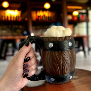 May include: A brown and black ceramic beer stein with a foam top. The stein has a handle and a metal band around the top.
