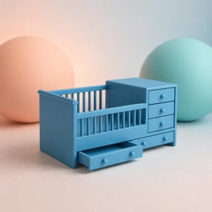 Puede incluir: Una cuna azul en miniatura con una cómoda incorporada. La cuna tiene barrotes verticales y un cajón extraído. La cómoda tiene cuatro cajones con pequeños pomos redondos. El fondo presenta dos grandes esferas de colores pastel.