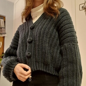 Könnte beinhalten: Ein dunkelblauer Strickcardigan mit V-Ausschnitt und Knopfleiste. Der Cardigan hat eine gerippte Struktur und lange Ärmel.