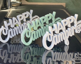 May include: Layered wooden signs with the words "HAPPY Camper" in a cursive font. The signs are in shades of gray and green, with a camper graphic on one. Perfect for camping enthusiasts.