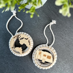 Op de afbeelding: Twee houten ornamenten met wit touw. Een ornament heeft een wereldkaart en de andere een camper.