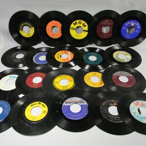 May include: A collection of 17 vintage 45 rpm vinyl records with various labels, including Decca, Columbia, M-G-M, RCA Victor, Peter Pan, ABC Paramount, and 20th Century Fox. The records are black with colorful labels.
