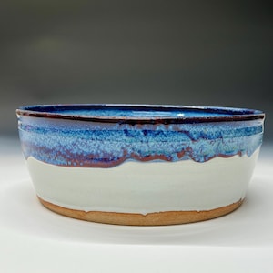 May include: A large, round ceramic bowl with a white glaze and a blue and purple glaze on the top. The bowl has a slightly rounded bottom.
