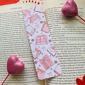 Peut inclure: Deux marque-pages roses et blancs avec un motif vichy rose et blanc. Les marque-pages présentent des piles de livres roses avec des nœuds blancs et des perles. Les marque-pages sont entourés d'étoiles blanches et de roses roses.