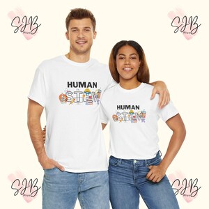 以下が含まれることがあります： 「HUMAN in STEM」の黒い文字が入った白いTシャツを着た2人。シャツにはカラフルなSTEM関連のグラフィックが描かれています。どちらもブルージーンズを着用しています。背景は薄いベージュ色です。