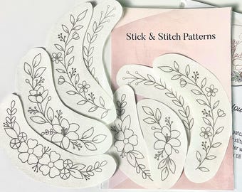May include: A set of six white fabric stick and stitch patterns featuring floral designs. The patterns are shaped like crescent moons and have the text "Stick & Stitch Patterns" printed on the background.