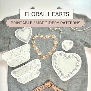 May include: Printable embroidery patterns for floral hearts. The patterns are on white paper and include a variety of heart shapes with floral details. The patterns are laid out on a gray sweatshirt.