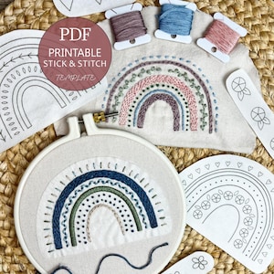 May include: An embroidery kit featuring a white fabric hoop with a stitched rainbow design, three spools of colored thread, and several paper templates with printed rainbow, heart, and flower patterns labeled PDF PRINTABLE STICK & STITCH.