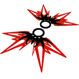 Pode incluir: Dois ornamentos decorativos pretos e vermelhos. Cada ornamento apresenta um design central preto com uma abertura circular, rodeado por formas vermelhas pontiagudas que irradiam para fora. Os ornamentos estão sobre um fundo branco.