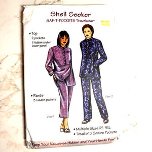 May include: A sewing pattern envelope titled Shell Seeker SAF-T-POCKETS Travelwear. It displays two illustrations of outfits: a solid purple top and pants set, and a blue floral print top and pants set. Text includes Multiple Sizes XS-3XL.