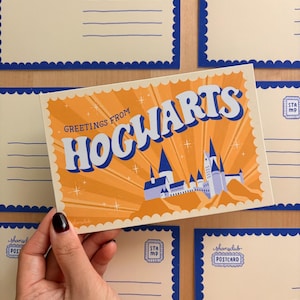 May include: A postcard featuring the words "GREETINGS FROM HOGWARTS" in blue against an orange background, with a castle illustration. The postcard has a blue scalloped border. Other postcards are visible.
