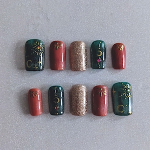 May include: Ten false fingernails in a green, gold and brown colour scheme. The nails feature a variety of designs including stars, moons and geometric shapes.