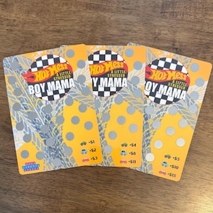 May include: Three yellow and black cards with the text "Hot Mess A Little Stressed Boy Mama" on the top card, "Hot Mess A Little Stressed Y Mama" on the middle card, and "Hot Mess A Little Stressed Oy Mama" on the bottom card. Each card has a grid of circles and numbers with dollar signs next to them.