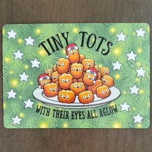 May include: A rectangular sign featuring a pile of golden-brown potato tots on a white plate. The tots have cartoon faces and some wear small Santa hats. The text reads TINY TOTS WITH THEIR EYES ALL AGLOW against a green pine needle background.
