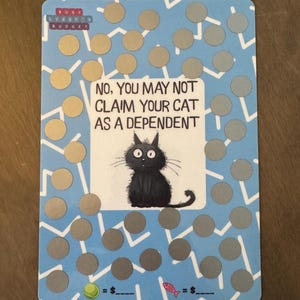 May include: A blue and white card with a cartoon black cat illustration and the text "NO, YOU MAY NOT CLAIM YOUR CAT AS A DEPENDENT." The card has a pattern of gold and silver circles.