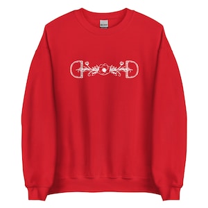 Könnte beinhalten: Roter Pullover mit einem weißen Design aus zwei Steigbügeln mit einer Blume in der Mitte.