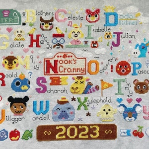 May include: A cross-stitch sampler featuring characters from Animal Crossing, with each letter of the alphabet represented by a character's name. The year 2023 is stitched at the bottom. The sampler includes various colors and designs.