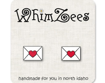 May include: A pair of earrings featuring a white envelope with a red heart inside. The earrings are handmade in North Idaho and are sold by the shop WhimsZeEs.