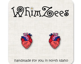 Puede incluir: Un par de pendientes de corazón anatómico rojo, rosa y azul. Los pendientes están hechos a mano en el norte de Idaho. "Whimzees" está escrito en la tarjeta.
