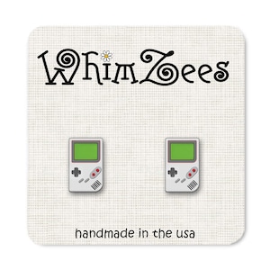 Op de afbeelding: Een paar zilverkleurige oorbellen in de vorm van een vintage draagbare videogameconsole. De oorbellen bevinden zich op een witte achtergrond met de tekst "Whimzees" en "handgemaakt in de VS".